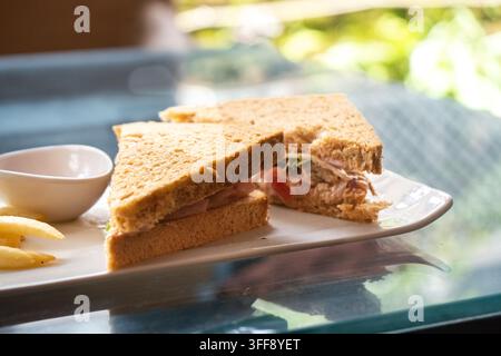 Panino con prosciutto integrale servito con patatine fritte croccanti e salsa da intingere su un piatto, creando un classico pranzo informale o un pasto comfort food. Foto Stock