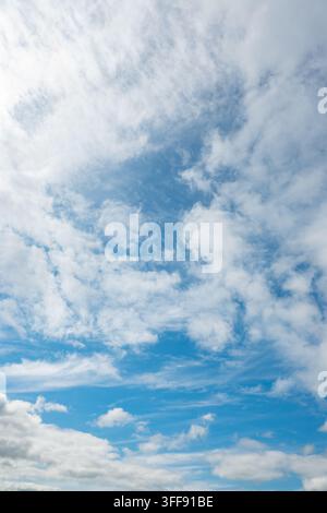 Un cielo blu brillante pieno di nuvole bianche sparse di varie forme e dimensioni. La luce naturale del giorno crea un'atmosfera fresca e aperta sull'ampia distesa Foto Stock