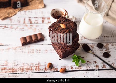 Brownie al cioccolato con condimento al cioccolato fuso, mandorle e foglie di menta con bicchiere di latte sul tavolo. Prodotti da forno, pasticceria Foto Stock