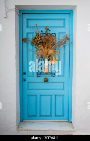 Vivace porta d'ingresso in legno blu adornata con un arrangiamento floreale essiccato e un mazzo di fiori appeso al centro, Altea, Alicante, Spagna Foto Stock