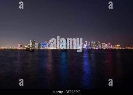 Doha, Qatar - 22 gennaio 2026: Vista notturna grandangolare dello skyline illuminato di West Bay attraverso la baia, con riflessi colorati della luce della città su Foto Stock