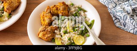 Una ciotola contiene pasta senza glutine con zucchine al forno, piselli e fagiolini insieme a nugget di pollo fritti. Questo pasto è servito su un piano di legno Foto Stock