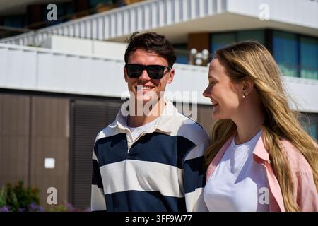 Giovane coppia sorridente che cammina insieme in una giornata soleggiata all'aperto. Foto Stock