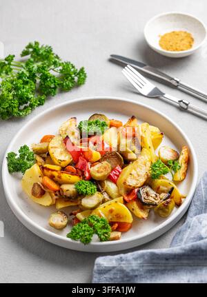 Verdure cotte al forno, patate, cavolo, peperone e cipolla su un piatto su uno sfondo chiaro con prezzemolo fresco. Concetto di piatto vegetariano. Foto Stock