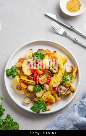 Verdure cotte a vapore patate, cavolo, pepe e cipolla in un piatto su uno sfondo chiaro con prezzemolo fresco. Concetto di dieta vegetariana. Vista dall'alto un Foto Stock