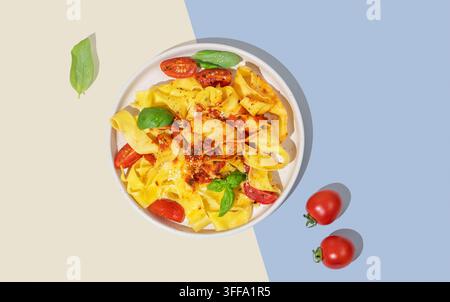 Tagliatelle o pappardelle con salsa di pomodoro, basilico e parmigiano su un piatto su uno sfondo giallo e blu con ombra. Concetto moderno o Foto Stock