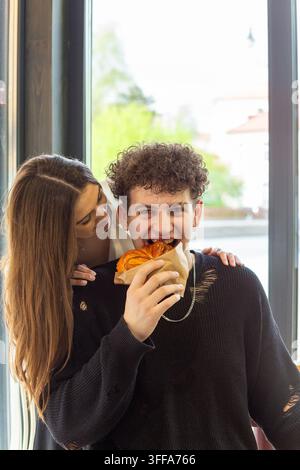 Una giovane coppia felice condivide un dolce in un accogliente caffè, catturando romanticismo, affetto e un giocoso appuntamento a base di cibo. Foto Stock