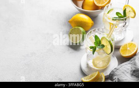 Due bicchieri di cocktail mojito con limone fresco, lime, menta e ghiaccio su uno sfondo chiaro con luce solare e frutta. Il concetto di un'estate alla moda Foto Stock