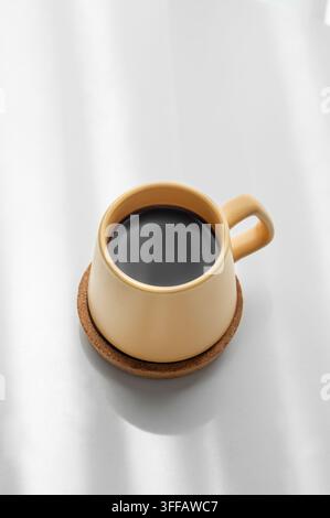 Caffè espresso appena preparato in una tazza gialla su sfondo bianco con luce del mattino. Concetto di una bevanda rinvigorente per la colazione per la pubblicità Foto Stock