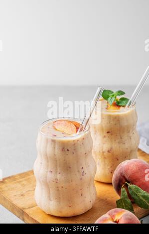 Due bicchieri di frullato con pesca e banana su una tavola di legno su uno sfondo chiaro con frutti tropicali. Concetto di alimentazione sana e dieta detox. Felice Foto Stock
