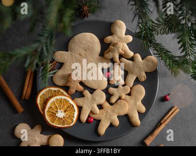 Biscotti di zenzero fatti in casa a forma di persone su un piatto nero, stile rustico, su uno sfondo scuro con rami di abete e bastoncini di cannella. Holida Foto Stock
