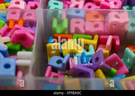 Perline alfabetiche colorate disposte in contenitori di stoccaggio trasparenti, che mostrano forme assortite e colori vivaci per il fai-da-te e la creazione di gioielli. Foto Stock