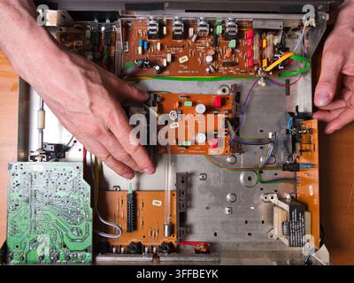 Mani che lavorano su un circ elettronico vintage - Vista dall'alto delle mani di una persona che ripara i componenti interni di un vecchio dispositivo elettronico, con Foto Stock