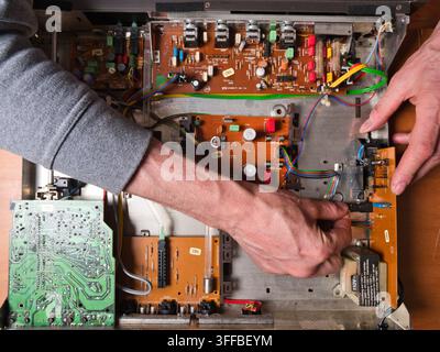 Mani che lavorano su un circ elettronico vintage - Vista dall'alto delle mani di una persona che ripara i componenti interni di un vecchio dispositivo elettronico, con Foto Stock