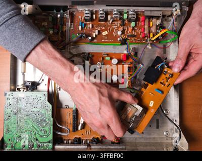 Mani che lavorano su un circ elettronico vintage - Vista dall'alto delle mani di una persona che ripara i componenti interni di un vecchio dispositivo elettronico, con Foto Stock