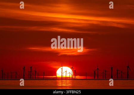 Parco eolico offshore silouettato contro un vivido tramonto rosso e arancione con il sole che tramonta sul mare a Talacre Beach, Flintshire, Galles del Nord Foto Stock