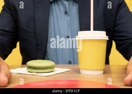 Concetto di colazione in un caffè di strada. Caffè con macarons su uno sfondo di legno. Un uomo d'affari fa colazione in un caffè, beve caffè e mangia qualcosa di dolce Foto Stock