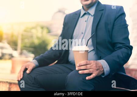 Affascinante uomo d'affari che si gode una pausa e beve caffè da asporto. Bicchiere di carta con caffè nella mano di un uomo Foto Stock