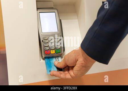 Mano maschile digita il codice PIN sul tastierino di una macchina per carte o terminale POS con carta di credito vuota inserita. Pagamento con carta di credito - uomo d'affari che tiene PO Foto Stock