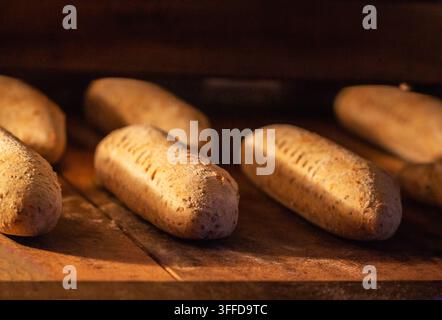 Vista ravvicinata di diversi pani oblungi che cuociono in un forno tradizionale. La crosta dorata si forma sui panini rustici, creando un aroma invitante di fr Foto Stock