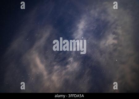 Inquadratura ampia che cattura il cielo notturno pieno di innumerevoli stelle e nuvole illuminate. Lo sfondo blu-nero profondo esalta la vastità e la bellezza del cosmo Foto Stock