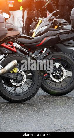 Fotografia verticale mostra due motociclette parcheggiate su asfalto bagnato. Il dettaglio evidenzia le ruote posteriori, i freni a disco, la sospensione, lo scarico. Gocce d'acqua su Foto Stock