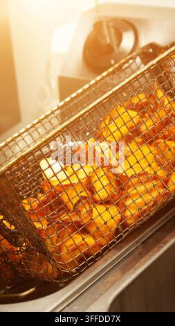 Dettaglio ravvicinato di patatine fritte calde e croccanti o wedges di patate in un cestello a maglie metalliche, appena rimosse dalla friggitrice, con l'olio che gocciola dalle patate cotte Foto Stock