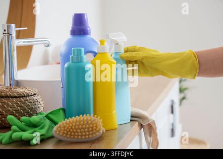 Pulizia della casa e manutenzione dell'igiene, persona con guanti di gomma gialli che sceglie prodotti per la pulizia su un ripiano del bagno per l'igiene domestica Foto Stock