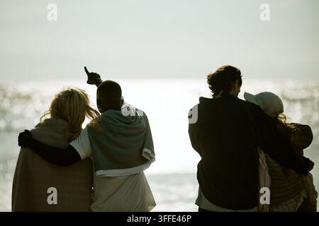 Amici multietnici che si abbracciano e guardano la spiaggia oceanica Foto Stock