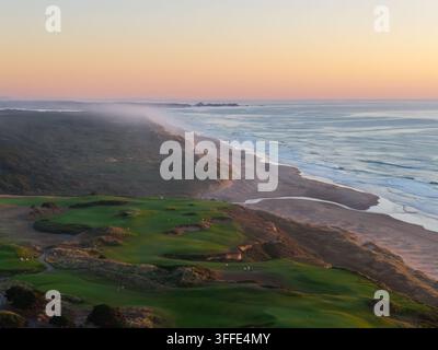 Vista aerea dei campi da golf di Bandon con lussureggianti fairway verdi lungo la costa frastagliata con la nebbia che scorre sulle dune al tramonto a Bandon, Oregon Foto Stock