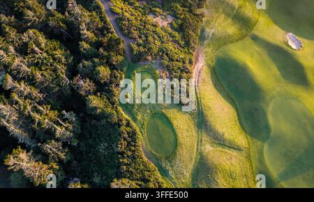 Vista aerea di una prospettiva drammatica dall'alto che cattura l'interazione di fairway verdi rigogliosi, bunker di sabbia e di una fitta foresta costiera a Bandon, Or Foto Stock