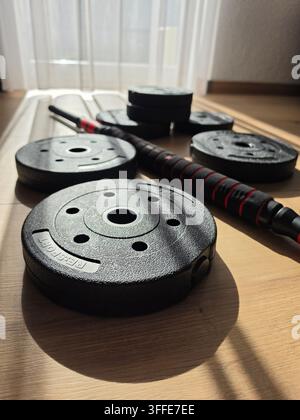 Piastre di peso in ghisa nera e bilanciere sul pavimento nella palestra di casa, primo piano dell'attrezzatura fitness per l'allenamento della forza Foto Stock