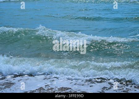 Primo piano di onde turchesi che si infrangono su sabbia bagnata con schiuma bianca Foto Stock