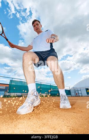 Uomo che gioca a tennis su campo di terra battuta in una veduta ad angolo basso Foto Stock