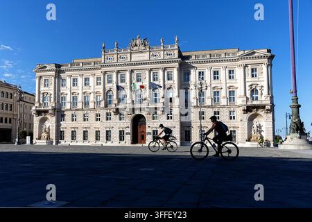 Una madre turista e suo figlio che pedalano davanti al maestoso palazzo neorinascimentale del Lloyd Triestino sul mare nella bella Trieste. Foto Stock
