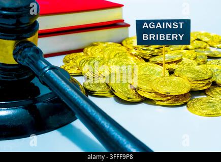 Martelletto del giudice con una pila di monete d'oro e testo contro la corruzione su una banconota. Concetto di lotta alla corruzione e rifiuto delle mazzette Foto Stock