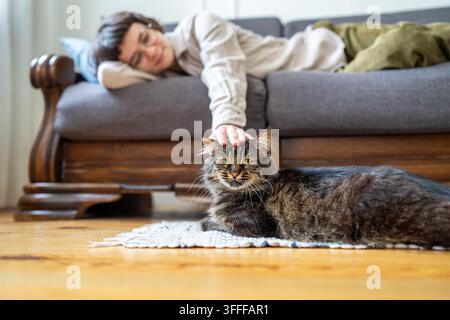 Giovane donna accarezza delicatamente il suo amato gatto a casa, trovando conforto attraverso l'affetto e il contatto tattile Foto Stock