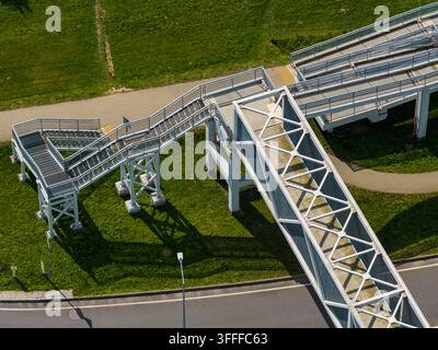 Vista aerea del moderno ponte pedonale con struttura a traliccio metallico e scale che si estende su una strada a Ziezmariai, Contea di Kaunas, Lituania. Foto Stock