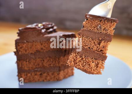 Prima piano di una forchetta che solleva una deliziosa fetta di ricco dolce al cioccolato fondente a strati Foto Stock