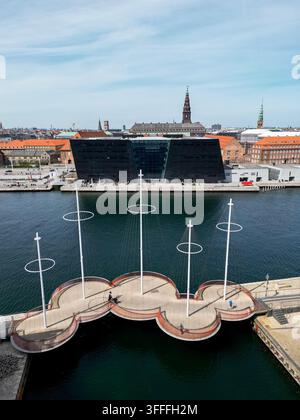 Vista aerea del ponte Cirkelbroen con piattaforme circolari e pali sopra l'acqua, con la Black Diamond Royal Library e l'architettura storica della città Foto Stock