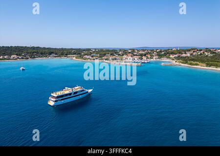 Vista aerea alta di una barca da escursione per passeggeri che si avvicina alla vivace baia turchese e al porto di Silba, Croazia. Un pittoresco villaggio insulare si trova Foto Stock