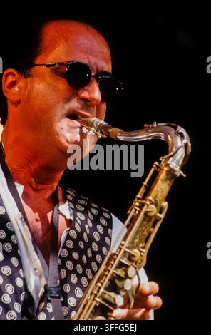 LONDON, UK - 27 GIUGNO 1993: Maestro di jazz fusion americano e sassofonista Michael Brecker in performance live sul palco con la Brecker Brothers band durante il festival Jazz on a Summer's Day tenutosi all'Alexandra Palace di Londra, Regno Unito, il 27 giugno 1993. Brecker è catturato in un ritratto ravvicinato nel mezzo di un assolo mentre suona il suo sassofono tenore, indossando occhiali da sole scuri e un distintivo gilet a motivi bianchi e neri sopra una camicia bianca con colletto. Questa fotografia a colori su pellicola 35 mm archivistica documenta la storica tournée di riunione della leggendaria coppia pluripremiata ai Grammy degli anni Novanta. Foto Stock
