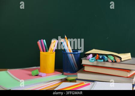 Diversi articoli di cancelleria e libri sul tavolo vicino alla lavagna, primo piano Foto Stock