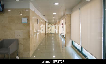 TORREVIEJA, SPAGNA – 27 AGOSTO 2026: Un corridoio dell'ospedale vuoto con pareti in marmo, pavimento piastrellato e un cartello della sala d'attesa che conduce verso un'uscita in Foto Stock