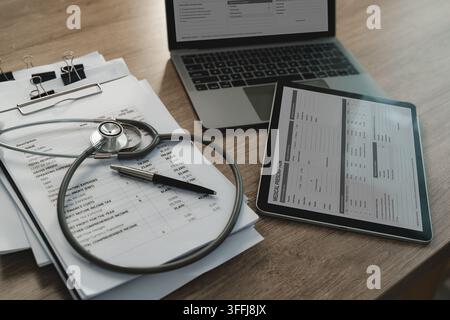 Stetoscopio, moduli di prescrizione medica e rapporto finanziario accanto a laptop e tablet per finanze sanitarie, spese mediche, contabilità e documentazione Foto Stock