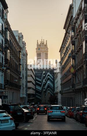 Madrid, Spagna: 7 apr. 2025 – Un’alta torre dell’orologio neogotica con guglie ornate si erge sopra edifici moderni alla fine di una stretta strada di Madrid piena Foto Stock