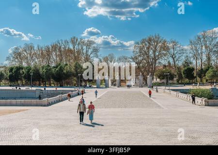 Madrid, Spagna: 7 apr. 2025 – Turisti e cittadini che passano davanti a una fila di pilastri di cancello in granito ornati sormontati da urne in pietra. Foto Stock