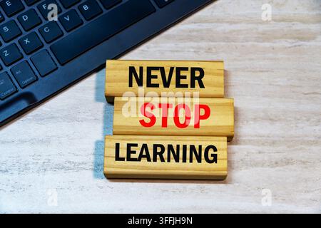 Testo « Never Stop Learning » scritto su blocchi di legno accanto alla tastiera di un laptop su uno sfondo di scrivania in legno. Concetto di formazione continua. Foto Stock