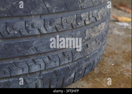 Primo piano di uno pneumatico di auto usato che mostra motivi dettagliati del battistrada, una superficie di gomma consumata, sporcizia e scanalature strutturate, evidenziando le condizioni e la struttura Foto Stock