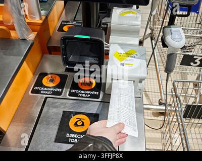 Kirov, Russia – 8 febbraio 2026: Un cliente utilizza uno scanner per codici a barre all'area della cassa per elaborare il pagamento della spesa al supermercato mentre riceve un rimborso Foto Stock